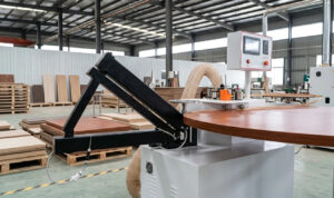Machine de détourage de bandes de bord de type rocker D5 industrielle effectuant un détourage de haute précision sur un plateau de table en bois incurvé dans un atelier de meubles.